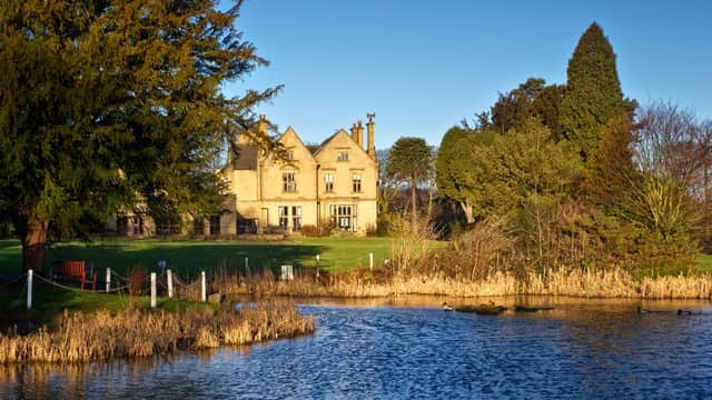 Historic Bagden Hall Hotel beside a tranquil lake, surrounded by greenery and trees under a clear blue sky.