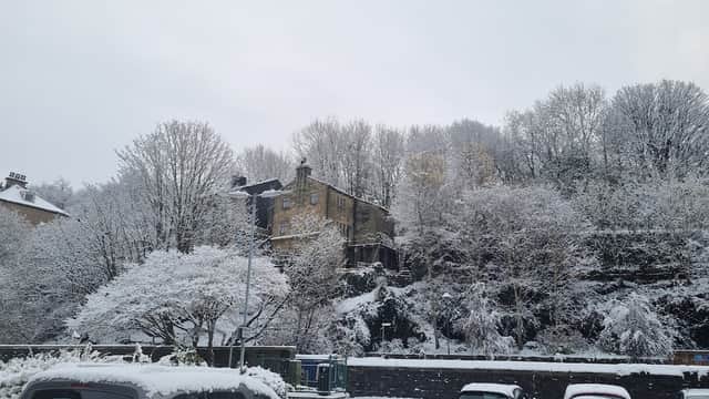 Snow-covered trees and a stone building overlook a car park filled with parked cars in Todmorden, Yorkshire.