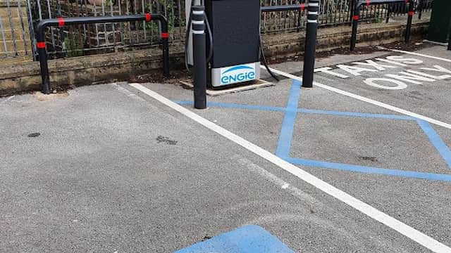 GeniePoint Charging Station with a blue EV charging symbol on the ground, surrounded by greenery and parked vehicles.