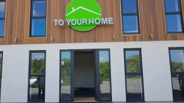 Modern shop exterior with large green sign "TO YOUR HOME" and large windows, located in Millhouse Green, Yorkshire.