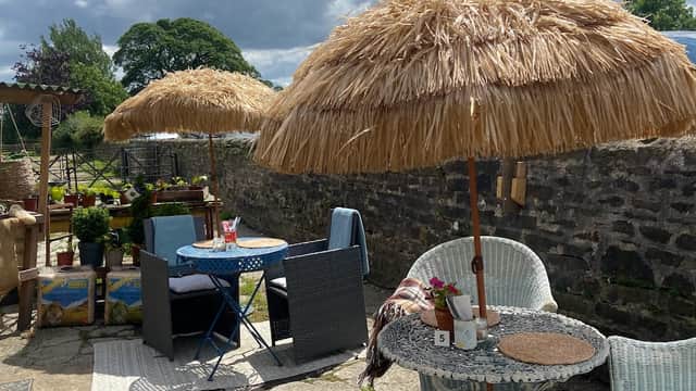 Thatched umbrellas shade outdoor seating at The Joyful Deli, surrounded by greenery and rustic stone walls.
