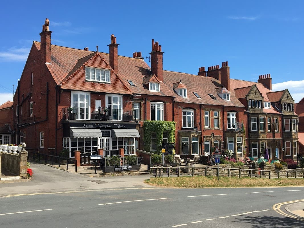 Charming guest house with red brick facade, balconies, and colorful flowers, set against a blue sky in Robin Hood's Bay.