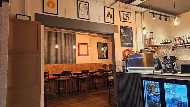 Cozy interior of Bottle and Bean with bar, seating, framed art, and illuminated shelves showcasing drinks.