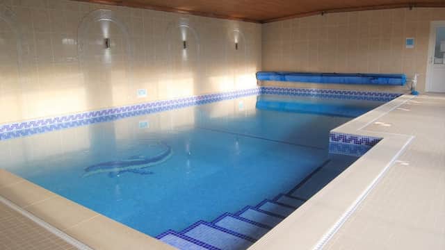 Indoor swimming pool with tiled edges, blue water, and wooden ceiling, featuring steps leading into the pool.