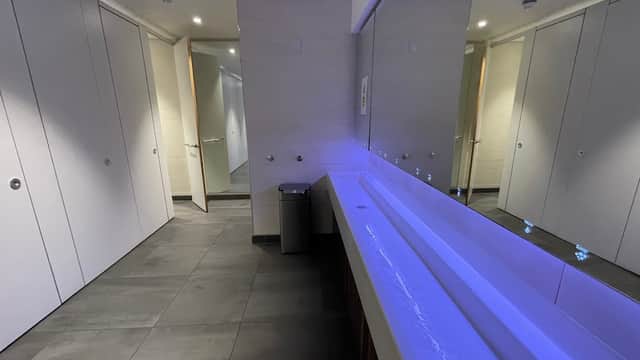 Modern public toilet interior with sleek stalls, a long sink, and ambient lighting. Clean and spacious design.