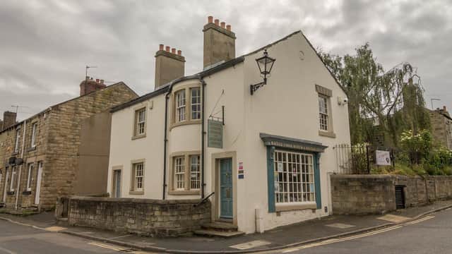 White building with blue door and window shutters, featuring a sign for Maurice Dobson Museum & Heritage Centre.
