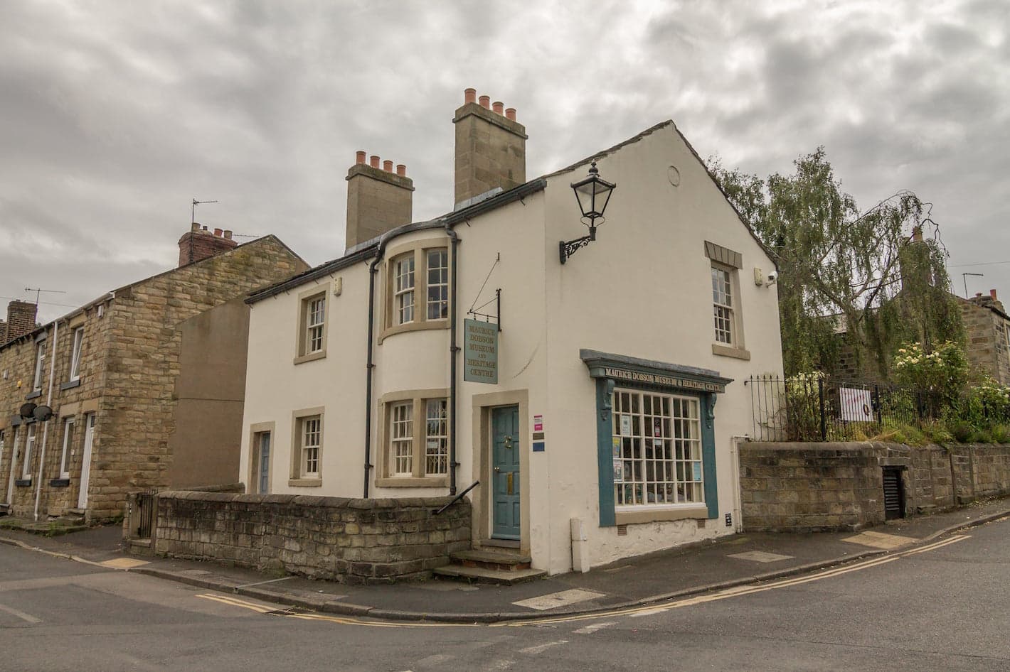 White building with blue door and window shutters, featuring a sign for Maurice Dobson Museum & Heritage Centre.