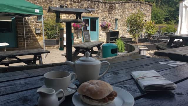 A rustic outdoor seating area with a table set for breakfast, featuring a tea set, a sandwich, and a menu.