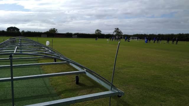 Sports field with green grass, goalposts, and players in training under a cloudy sky.