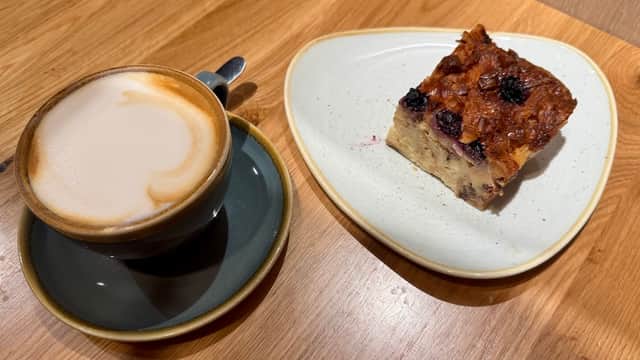 Coffee in a dark cup next to a slice of fruit-topped cake on a plate, set on a wooden table.