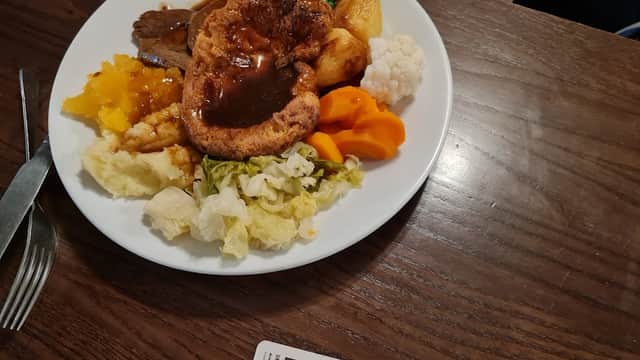 A plate of traditional roast dinner with Yorkshire pudding, vegetables, and gravy on a wooden table.