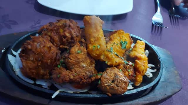 Sizzling platter of assorted fried appetizers, garnished with herbs, on a wooden serving board.