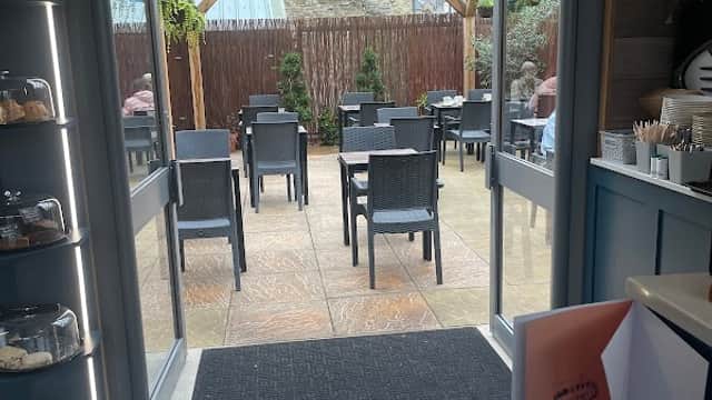 Open doors leading to a patio with tables and chairs, surrounded by greenery and a wooden pergola.