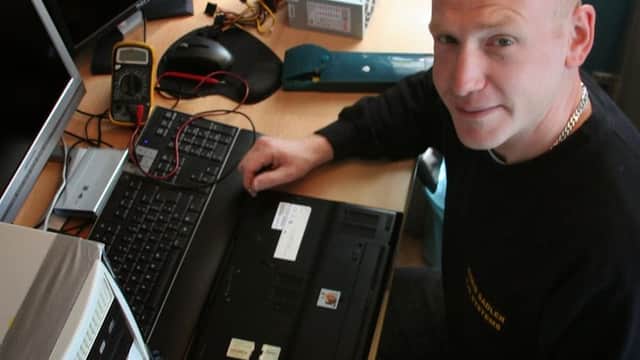 A man working on a laptop at a desk with monitors, tools, and computer components in a tech workspace.