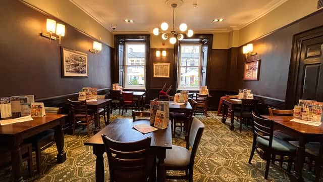 Cozy restaurant interior with wooden tables, chairs, and patterned carpet, featuring large windows and warm lighting.