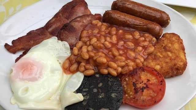 A plate featuring a full English breakfast: bacon, sausages, baked beans, fried egg, hash brown, black pudding, and tomato.