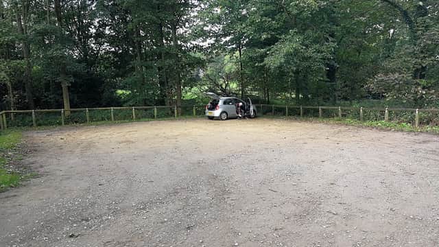 Gravel car park surrounded by trees, with a parked car near a wooden fence in a quiet, natural setting.