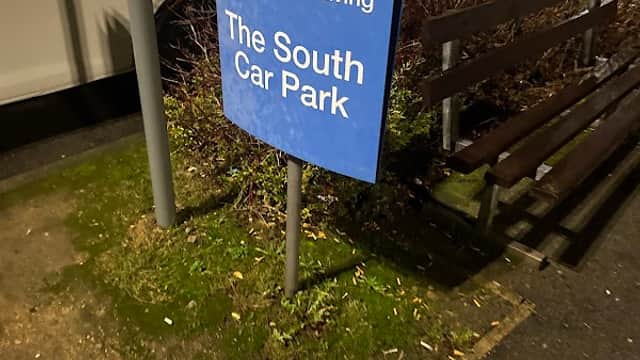Sign indicating "You are now leaving The South Car Park," surrounded by greenery and parked cars.
