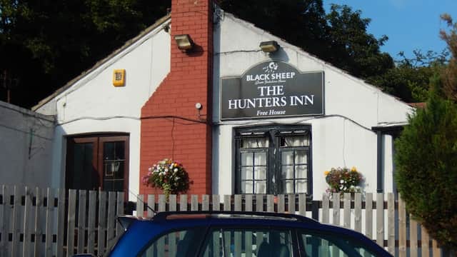 Hunters Inn bar with a sign, red brick chimney, flower baskets, and wooden fencing in Leathley, Yorkshire.