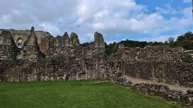 Ruins of Rievaulx Abbey with stone walls, grassy areas, and a partly cloudy sky in Yorkshire.