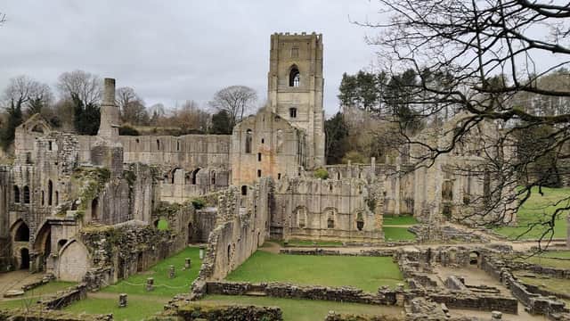 Ruins of Fountains Abbey with stone walls, archways, and grassy areas under a cloudy sky in Ripon, Yorkshire.
