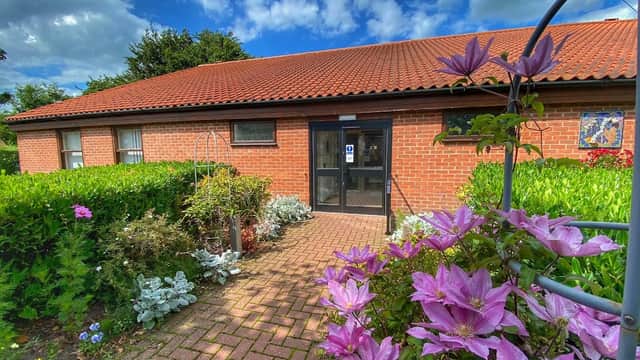 Wilberfoss Community Centre entrance surrounded by colorful flowers and greenery under a partly cloudy sky.