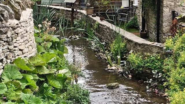Maltongate Parking near a tranquil stream, surrounded by lush greenery and charming stone buildings in Thornton-le-Dale.