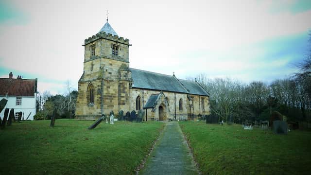 Historic stone church with a tall tower, surrounded by gravestones and trees in a rural setting.