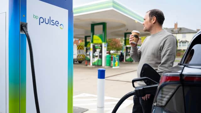 A man holds a coffee while charging an electric vehicle at a bp pulse charging station in Harden, Yorkshire.
