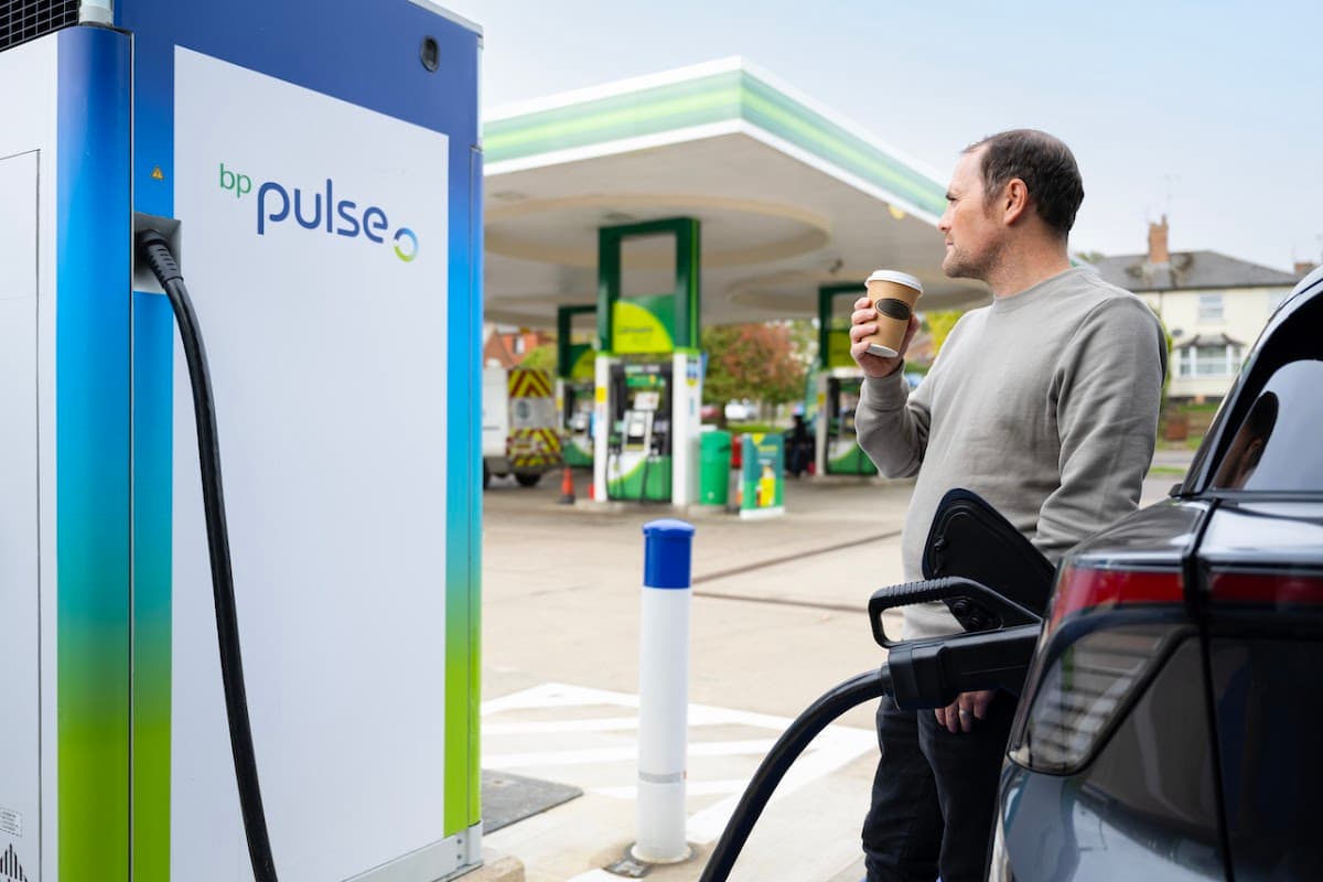 A man holds a coffee while charging an electric vehicle at a bp pulse charging station in Harden, Yorkshire.