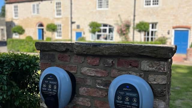 Pod Point charging station mounted on a brick wall, with traditional houses and blue doors in the background.