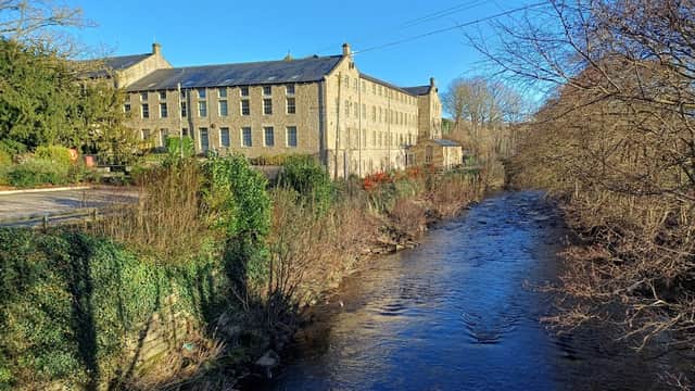 Flax Mill Cottage beside a river, featuring a historic stone building and lush greenery in a scenic landscape.
