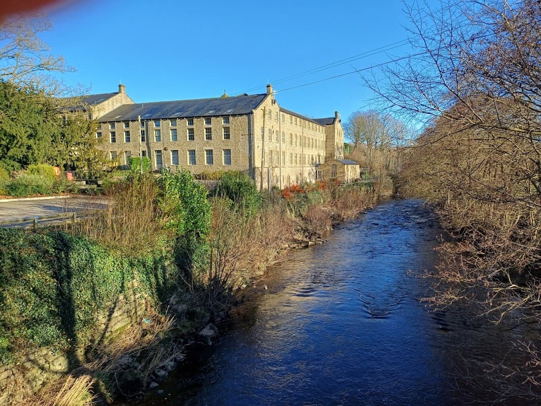 Flax Mill Cottage beside a river, featuring a historic stone building and lush greenery in a scenic landscape.