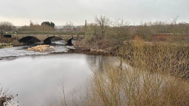 A tranquil river scene with a stone bridge, bare trees, and overcast skies in Ossett, Yorkshire.