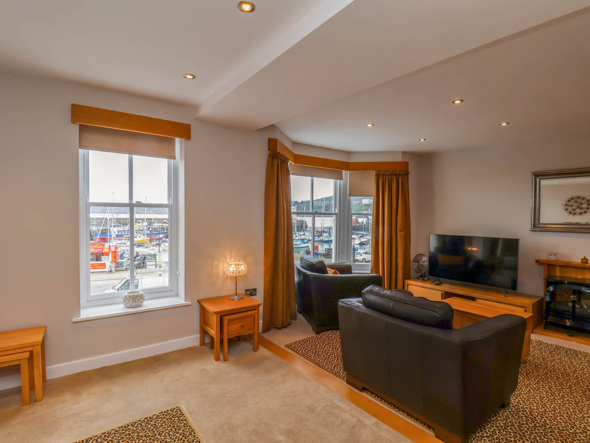 Cozy living room with large windows, harbor view, leather sofas, and warm lighting.