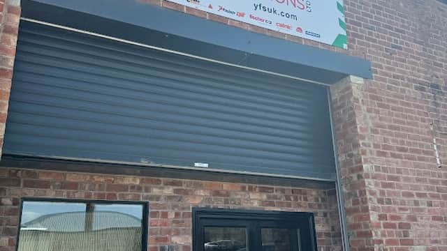 Sign for Yorkshire Fixing Solutions Ltd above a large black roller shutter door on a brick building.