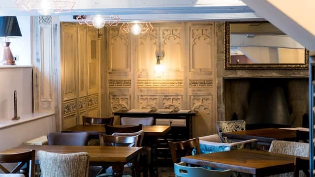 Cozy bar interior with wooden tables, upholstered chairs, ornate wall paneling, and warm lighting fixtures.