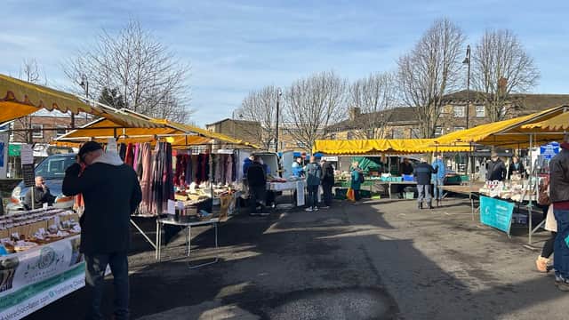 Stalls with colorful canopies displaying goods in a bustling car park, surrounded by bare trees and clear blue skies.