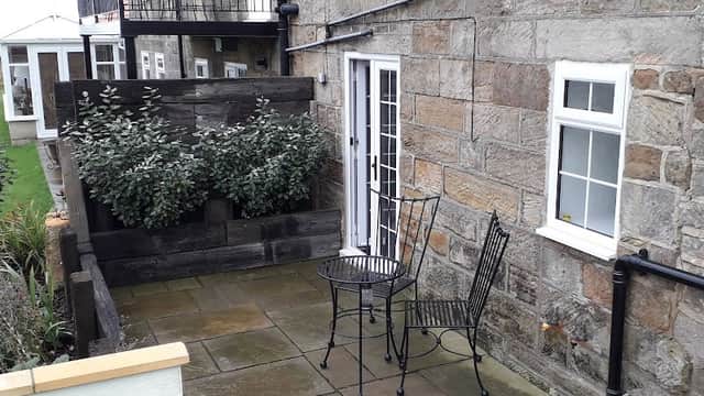 Stone exterior of Alum House with a small patio, black metal table and chairs, and greenery in planters.