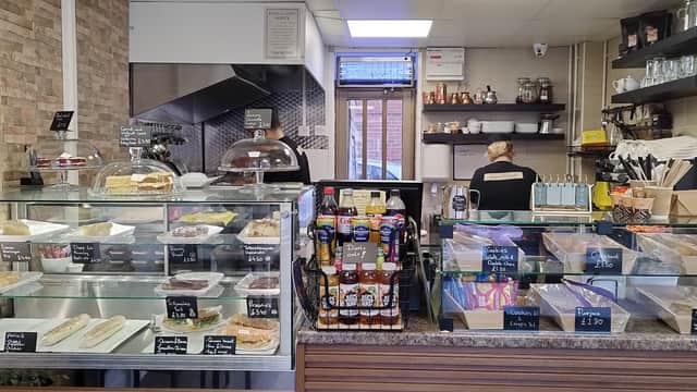 Counter display with cakes, pastries, drinks, and a barista behind the counter in a cozy cafe setting.