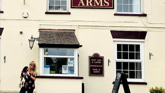 Historic hotel facade with "ROOS ARMS" sign, a woman holding a dog, and a blackboard menu outside.