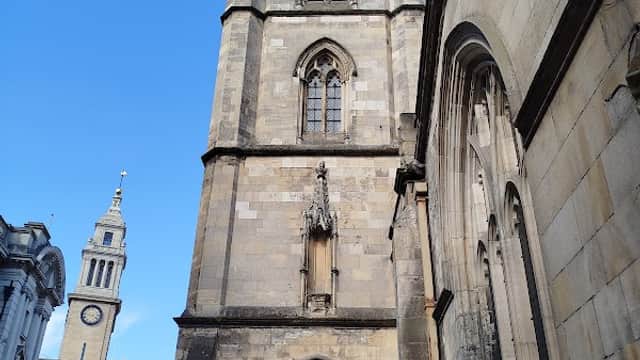 Tall stone tower with gothic architecture, flanked by buildings and a clear blue sky in Hanover Square, Hull.