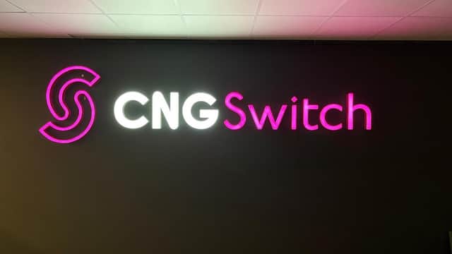 Neon sign of "CNG Switch" in pink and white against a dark wall, with a modern design and illuminated letters.