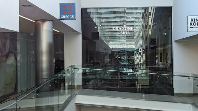 Central Arcade interior featuring glass railings, shops, and signage for Greggs and Dragonfly Skin.