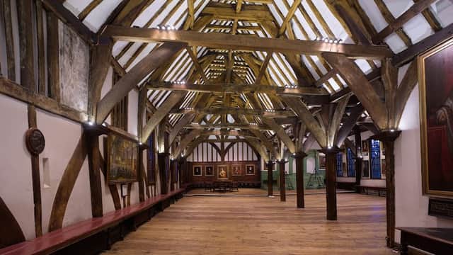 Spacious hall with wooden beams, benches along the walls, and framed paintings in a historic setting.