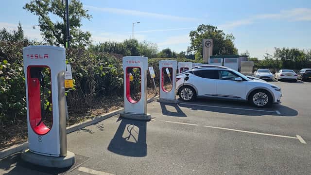 Tesla Supercharger station with charging units and a parked Tesla vehicle in a sunny parking lot.