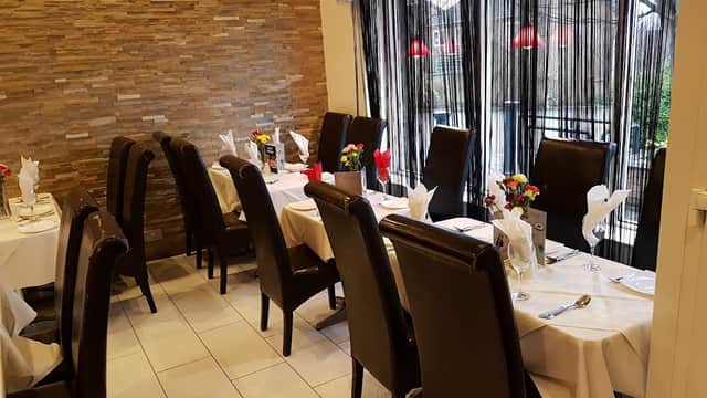 Cozy dining area with brown leather chairs, white tablecloths, flowers, and large windows draped with sheer curtains.
