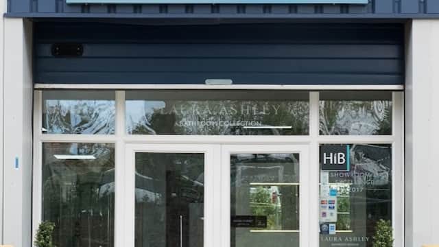Modern storefront with "Sanctuary Bathrooms" sign, glass doors, and potted plants flanking the entrance.