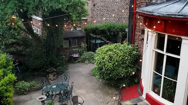 Charming courtyard with tables, chairs, and string lights surrounded by greenery and historic brick buildings.