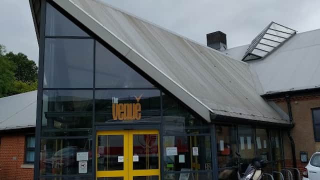 Modern building with a slanted roof, large glass entrance, yellow doors, and signage reading "The Venue."